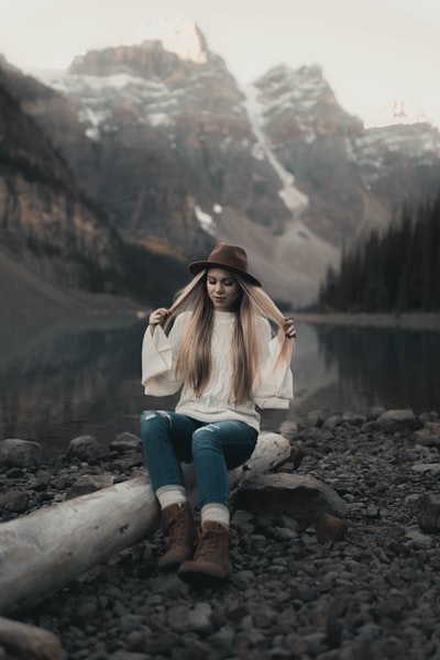 女人穿着白色夹克和蓝色牛仔裤坐在岩石白天湖附近
